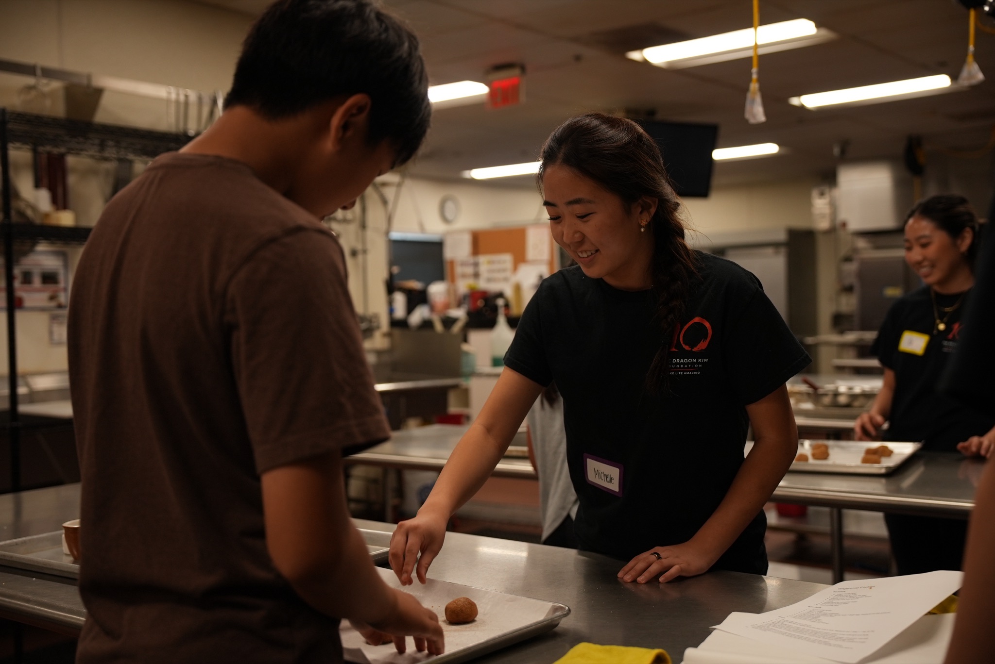 Michelle smiling as she guides a young student through shaping dough